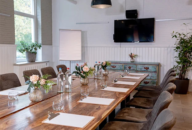 Vergaderruimte in Den Haag met lange tafel, tv en notitieblokken voor zaalverhuur