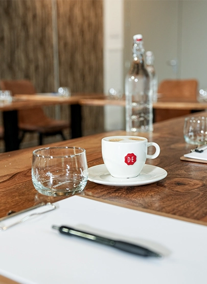 Vergadertafel met koffie, water en schrijfmaterialen in een professionele vergaderruimte.