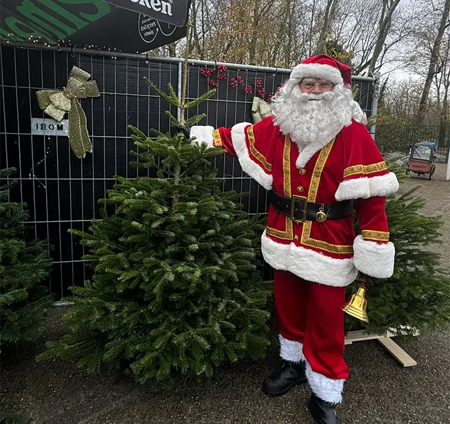 De kerstman die naast een kerstboom staat.